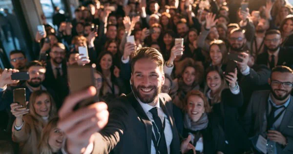 Man taking a selfie with a large crowd of people holding up their phones