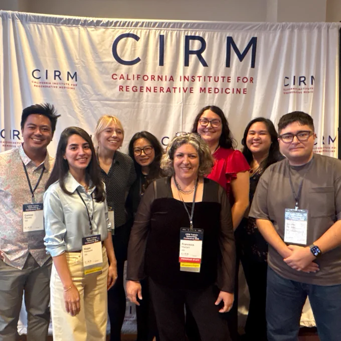 A group of nine people smiling in front of a banner for the California Institute for Regenerative Medicine (CIRM).