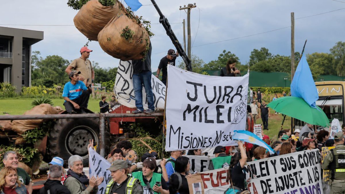 puellaok's tweet photo. Así recibe Misiones a Milei: con tractores, camiones y un pueblo entero copando las rutas para frenar el saqueo a las economías regionales. Mientras viaja para disertar ante gerentes de finanzas, afuera la realidad lo destruye: familias enteras y productores fundidos por un modelo que arrasó con todo. Vaya a donde vaya, la bronca lo persigue y los carteles de los estafados sonlapura verdad: "Creíamos en vos y hoy nos arrepentimos".