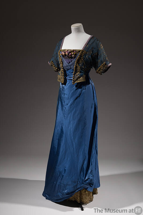 plummie9's tweet photo. London & New York
Lucile 
( Lucy Christiana, Lady Duff-Gordon, 1863-1935)

Evening Dress, c. 1912

" Blue silk taffeta gown; blue sheer silk bodice with gold thread embroidered  design; short kimono sleeve, mock bolero front; blue chiffon surplice  empire front with blue modesty piece trimmed with gilt lace.
Mauve  ribbon flowers; flared skirt caught up at either side hem; beige  petticoat attached, gilt lace at hem; centre back self streamer; centre  back hook closing.

A survivor of the Titanic, Lady Duff  Gordon, the designer known simply as Lucile, was one of the most  innovative couturiers of the Edwardian era."
@FIT 
#FashionHistory