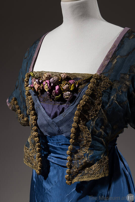 plummie9's tweet photo. London & New York
Lucile 
( Lucy Christiana, Lady Duff-Gordon, 1863-1935)

Evening Dress, c. 1912

" Blue silk taffeta gown; blue sheer silk bodice with gold thread embroidered  design; short kimono sleeve, mock bolero front; blue chiffon surplice  empire front with blue modesty piece trimmed with gilt lace.
Mauve  ribbon flowers; flared skirt caught up at either side hem; beige  petticoat attached, gilt lace at hem; centre back self streamer; centre  back hook closing.

A survivor of the Titanic, Lady Duff  Gordon, the designer known simply as Lucile, was one of the most  innovative couturiers of the Edwardian era."
@FIT 
#FashionHistory