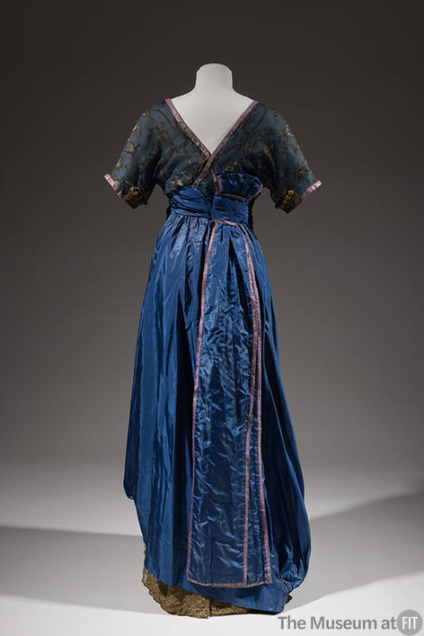 plummie9's tweet photo. London & New York
Lucile 
( Lucy Christiana, Lady Duff-Gordon, 1863-1935)

Evening Dress, c. 1912

" Blue silk taffeta gown; blue sheer silk bodice with gold thread embroidered  design; short kimono sleeve, mock bolero front; blue chiffon surplice  empire front with blue modesty piece trimmed with gilt lace.
Mauve  ribbon flowers; flared skirt caught up at either side hem; beige  petticoat attached, gilt lace at hem; centre back self streamer; centre  back hook closing.

A survivor of the Titanic, Lady Duff  Gordon, the designer known simply as Lucile, was one of the most  innovative couturiers of the Edwardian era."
@FIT 
#FashionHistory
