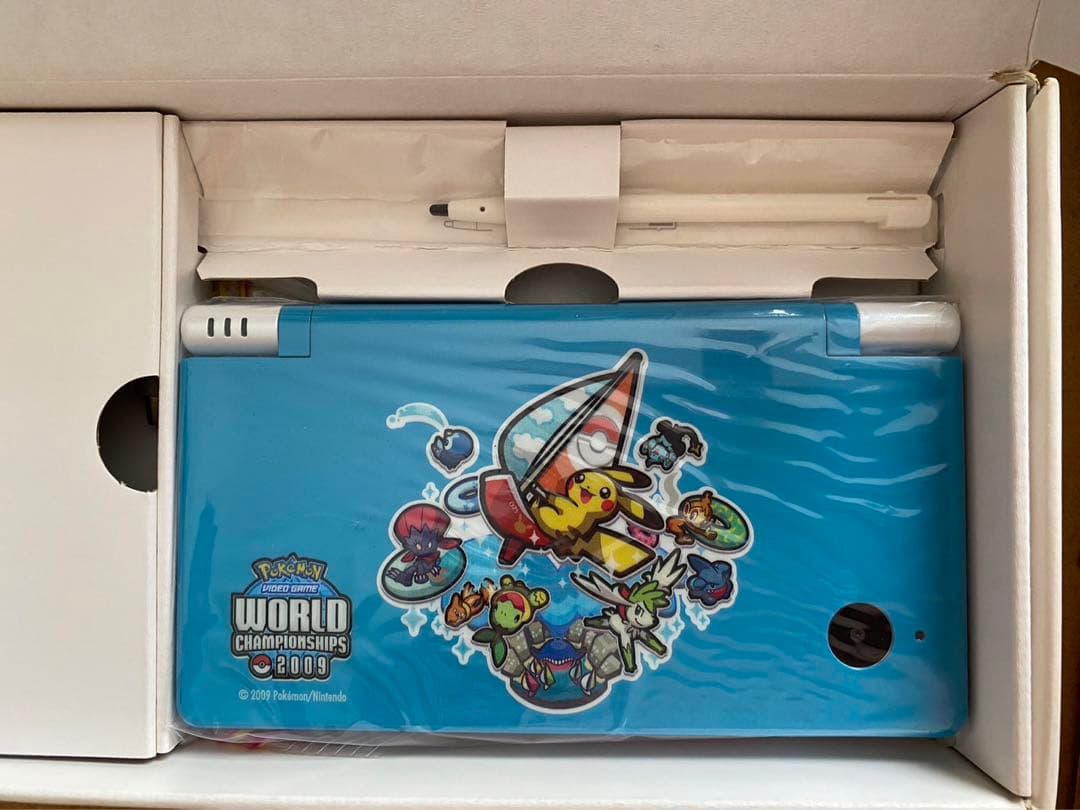 AmigaPrime's tweet photo. 優勝者にしか渡らないゲーム機が、実は普通のDSiの上から塗っただけだったという話。

2009年のポケモン世界大会、サンディエゴ開催。本戦まで勝ち残った選手にだけ配られた限定本体で、数は100台強。

水色のフタにピカチュウが帆船で駆けてる絵。塗装が厚いのか、市販の保護カバーがギリ入らない。

箱に入ったままの個体もまだ残ってて、同梱のタッチペンまで大会仕様の塗装。勝った人だけが知ってる仕上がりってやつ。

こんなの持ってる人、日本にほんの数人のはず。