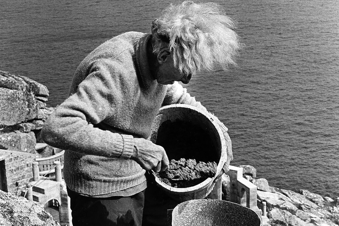 timelessbritain's tweet photo. Cornwall’s Minack Theatre looks as if it has been carved into the cliffs for centuries. In 1931, it was still a rough gully of gorse and granite above a 90-foot drop to the sea.

The change began because Rowena Cade wanted somewhere for a local group to perform Shakespeare.

She had moved to Cornwall after the First World War and bought the Minack headland for £100. In 1929 she helped with an outdoor production of A Midsummer Night’s Dream in a nearby valley. When the group decided to stage The Tempest next, Rowena offered the cliff at the bottom of her garden.

There was one problem. There was no theatre.

So Rowena and her helpers started making one.

Her gardener Billy Rawlings and another local man cut huge granite boulders by hand. They worked with bars, hand tools and, sometimes, dynamite on a slope where one bad step could have meant a fall into the sea.

Rowena filled the gaps with earth and stone. She carried sacks of sand up from the beach to mix into concrete. The first audience arrived for The Tempest in 1932, with the young theatre lit by battery lamps and car headlights.

That could have been the end of it.

Instead, she kept building.

Year after year, Rowena added terraces, steps, seats and strange little details that made the place hers. She pressed patterns into wet concrete with an old screwdriver. Many of the seats still carry the names and dates of productions performed there.

She continued working on the Minack well into her eighties.

I assembled these images because the finished theatre can hide the hardest part of its story. What looks like an ancient amphitheatre was shaped, altered and cared for across one woman’s lifetime, with a few helpers, simple tools and a cliff that never became any less steep.

The Minack is still a working theatre. It welcomes more than 200,000 visitors a year and stages more than 200 live performances, from plays and opera to music and children’s shows.

That is why this place is worth remembering. It was not inherited complete from some distant age. It was made because one woman looked at an awkward Cornish cliff and decided it could become a stage.

The sea is still behind it. The granite is still under it. And every time an audience takes its seats, Rowena Cade’s unlikely theatre does exactly what she built it to do.