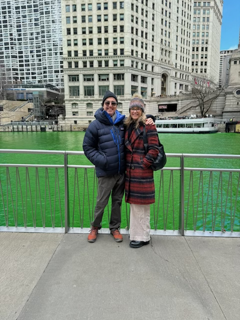 A couple poses in front of the Chicago River, which is dyed green.