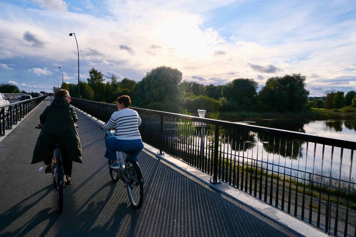 Cyclists in casual autumn attire ride along dedicated cycling infrastructure lined with buildings and trees on the streets of Tallinn, Estonia.