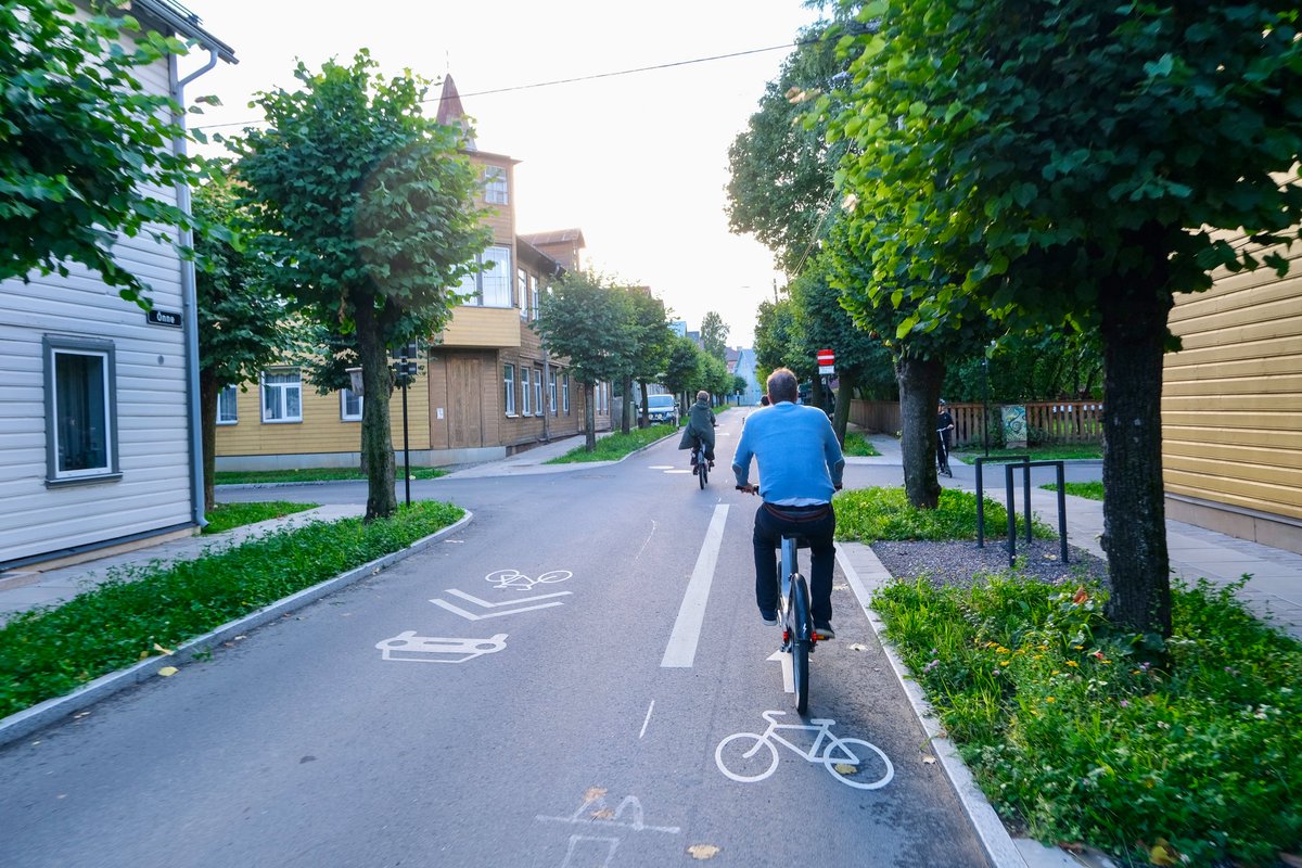 Cyclists in casual autumn attire ride along dedicated cycling infrastructure lined with buildings and trees on the streets of Tallinn, Estonia.