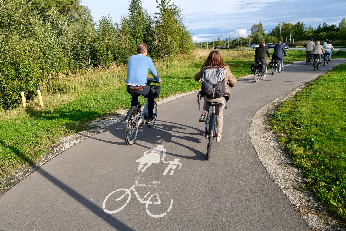 Cyclists in casual autumn attire ride along dedicated cycling infrastructure lined with buildings and trees on the streets of Tallinn, Estonia.