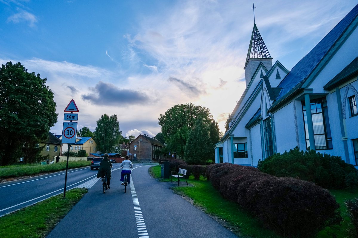 Cyclists in casual autumn attire ride along dedicated cycling infrastructure lined with buildings and trees on the streets of Tallinn, Estonia.