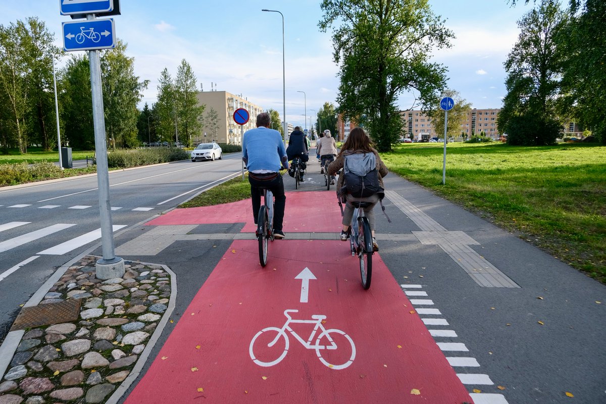 Cyclists in casual autumn attire ride along dedicated cycling infrastructure lined with buildings and trees on the streets of Tallinn, Estonia.