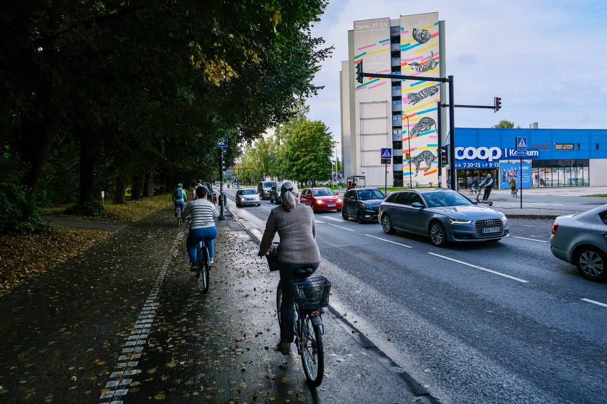 Cyclists in casual autumn attire ride along dedicated cycling infrastructure lined with buildings and trees on the streets of Tallinn, Estonia.