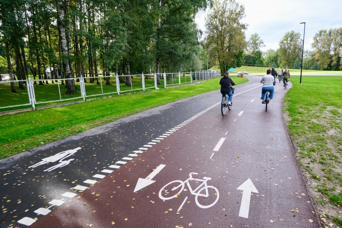 Cyclists in casual autumn attire ride along dedicated cycling infrastructure lined with buildings and trees on the streets of Tallinn, Estonia.
