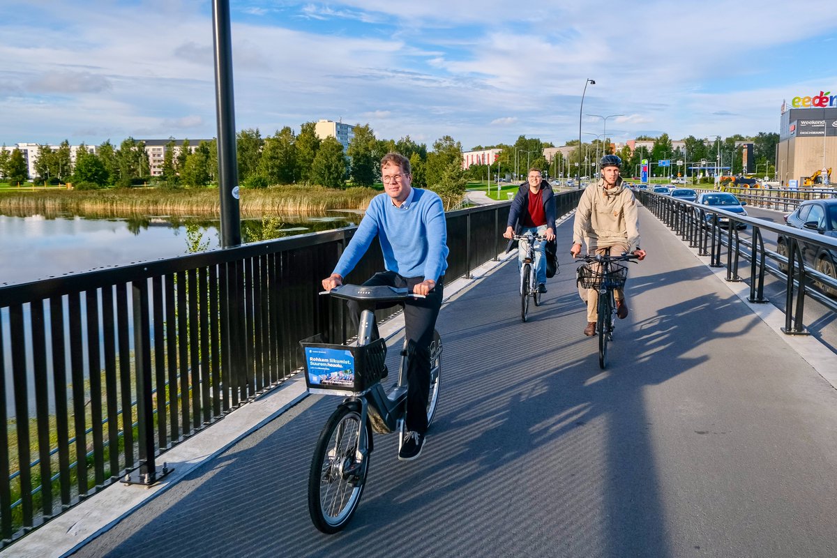 Cyclists in casual autumn attire ride along dedicated cycling infrastructure lined with buildings and trees on the streets of Tallinn, Estonia.