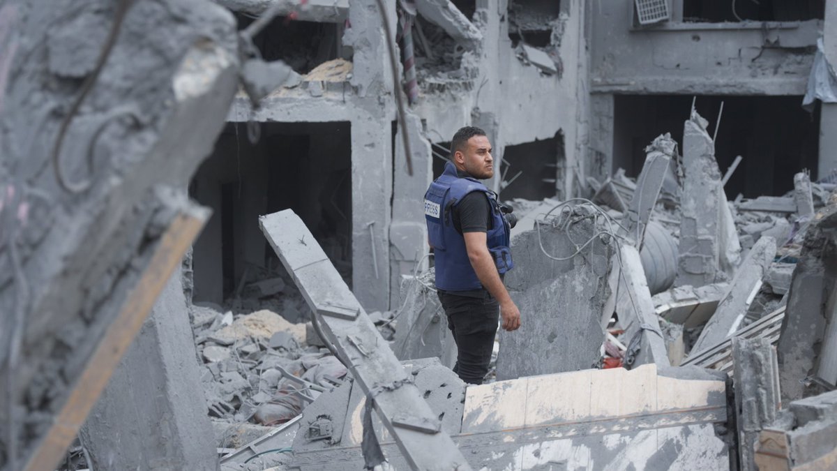 A still from the film Citizen Osama showing a Palestinian journalist wearing a press vest and standing in the rubble of a building in Gaza.