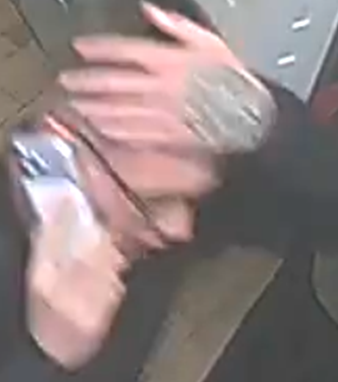 A blurry, high-angle security camera shot of a person holding a phone to their ear with a tattoo visible on their hand.