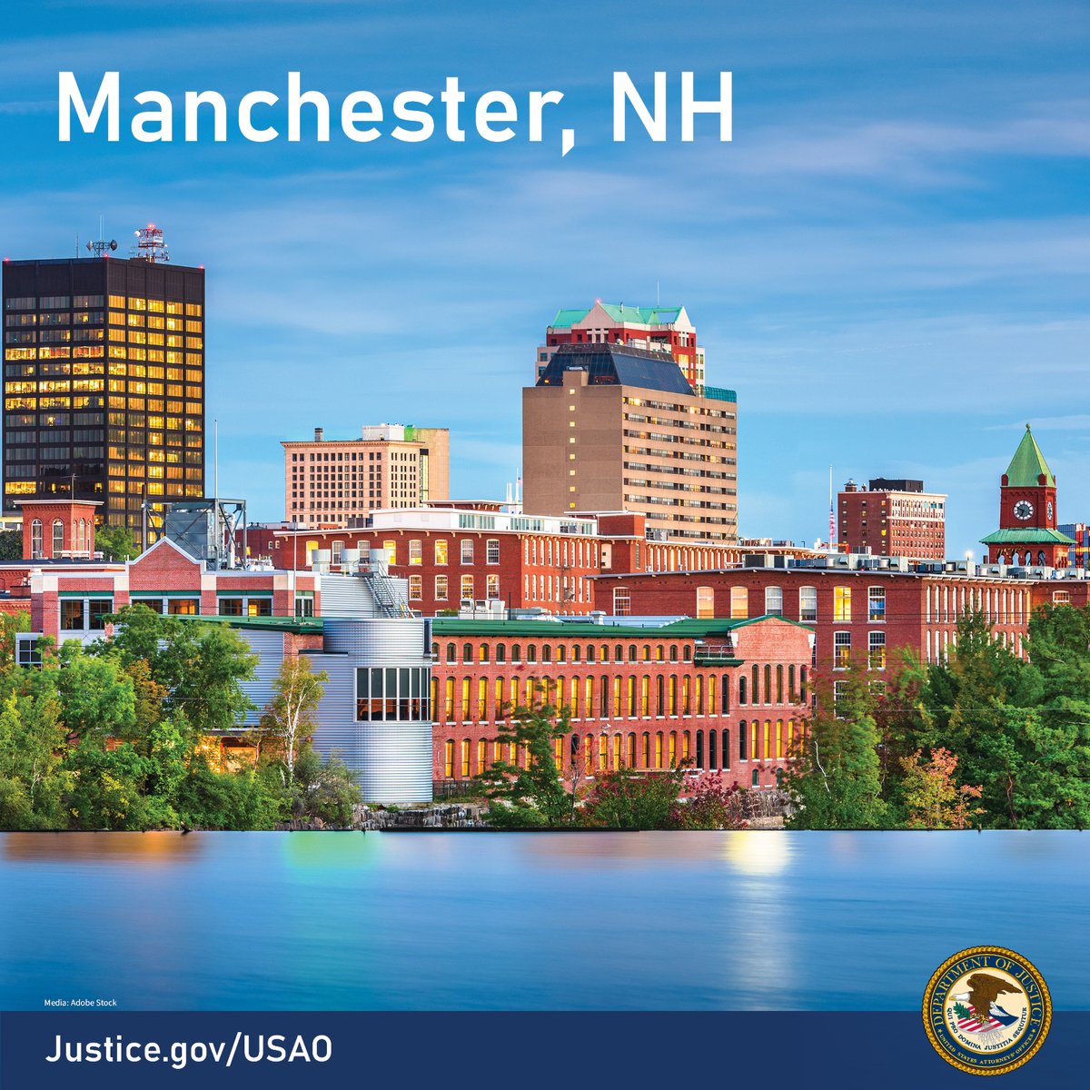 Manchester, NH. A still body of water sits in front of several buildings of different heights. There are a few trees between the water’s edge and the buildings. The sky is a dark blue with hints of clouds and many of the buildings are red brick. http://Justice.gov/USAO
