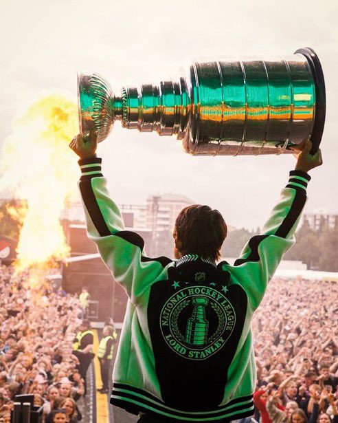 Photo of Sebastian Aho’s back while he holds the Cup above his head on stage at a music festival in Finland during his day with the Cup