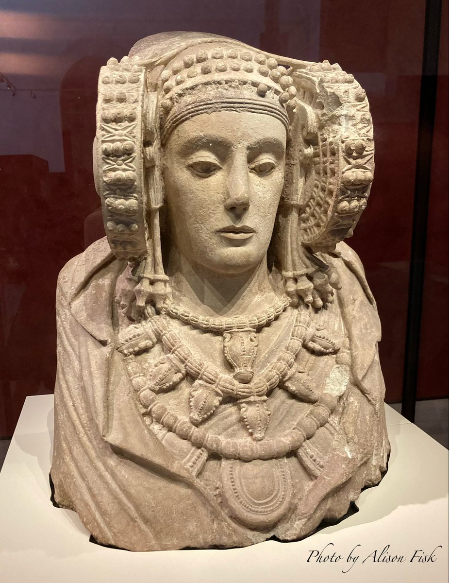 My photo shows a famous Iberian limestone sculpture known as ‘La Dama de Elche’ / The Lady of Elche, on display at the National Archaeological Museum in Madrid. Here is a description by the museum:
“Female bust that features a lady's face with very perfect features and that preserves traces of polychromy on the lips and specific areas of face and clothing. The lady is richly dressed: on her head she wears a headdress formed by a pointed tiara covered by a veil and on top of it a strap that joins the two side “cases" that frame the face, where the hairstyle and a headband would be collected on the forehead; the back and shoulders are covered with a mantle that forms folds on the front and exposes three necklaces with amphoras and amulet holders; the earrings hang either side of the face, and a small fibula closes the tunic on the neckline. It was richly painted with red, blue and yellow tones and application of gold sheets, of which hardly any traces remain.