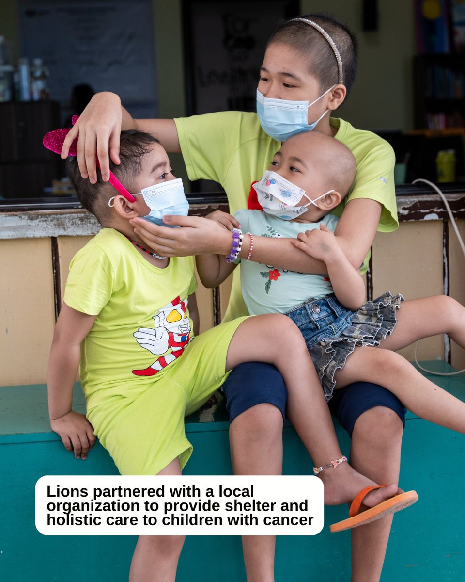 Children wearing face masks sit together on a bench. They share a moment of closeness, with one child placing a hand on another's head. The children are dressed in colorful clothes, and one shirt features a cartoon character. A text overlay states that Lions partnered with a local organization to provide shelter and holistic care to children with cancer.