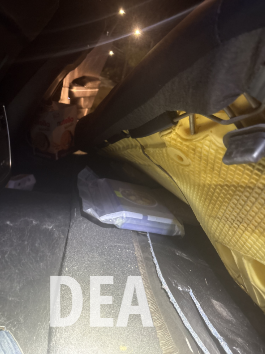 View under a car seat showing a yellow foam cushion and a plastic container on the floor with 'DEA' text overlay. Suspected fentanyl powder.