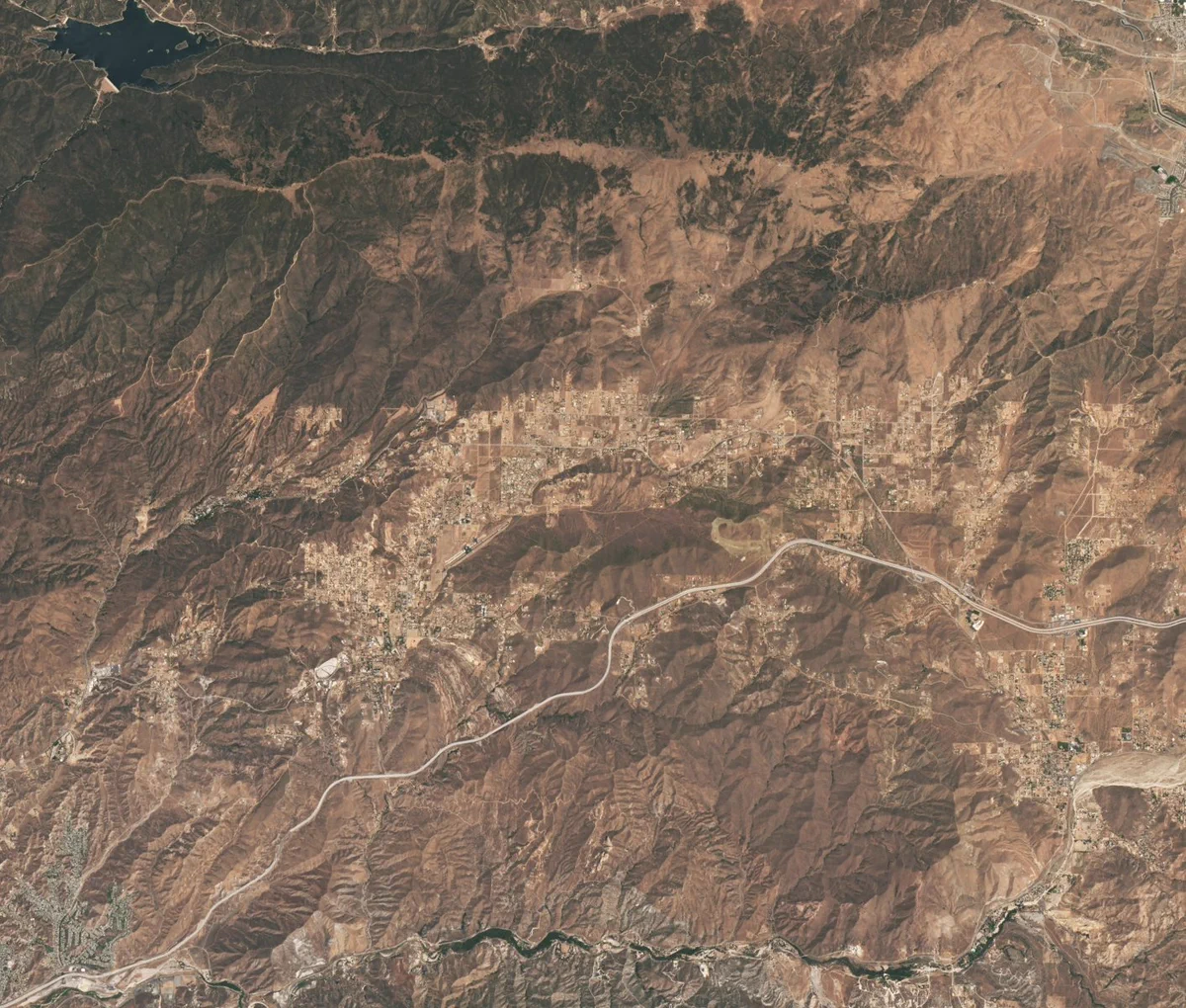 Natural color satellite image showing the Vasquez Rocks Natural Area and surrounding area in Southern California. Most of the landscape is brown and mountainous.The Vasquez Rocks appear as a patch of curved gray stripes just below and to the left of center near Agua Dulce. Palmdale is barely visible in the top right corner and the Bouquet Reservoir is near the top left corner. Credit: NASA