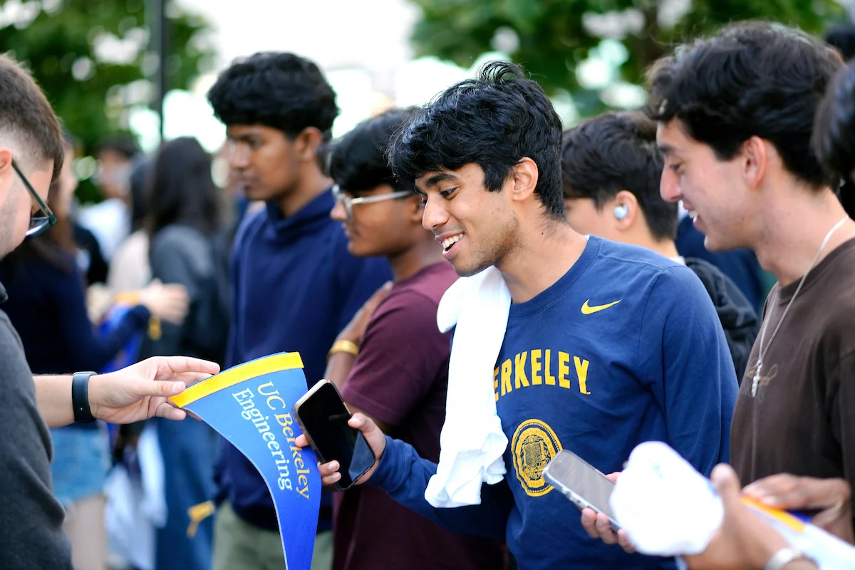 An attendee in a blue Berkeley long sleeve is handed a wall flag that says “UC Berkeley Engineering.” 
