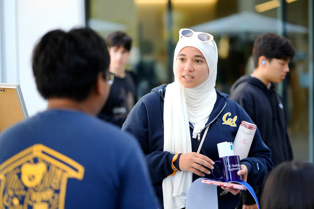 Two students in conversation as one holds Berkeley Engineering items. 