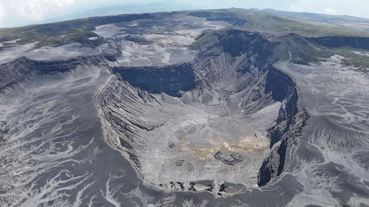 vulcaniya's tweet photo. Ngazidja, Union of the Comoros, 9 September 2026

Ngazidja, the largest island of the Comoros, is a single landmass made by two shield volcanoes that have behaved in almost opposite ways. Mount Karthala occupies the southern two thirds and has erupted more than twenty times since the nineteenth century. La Grille builds the northern third, carries several hundred scoria cones on its slopes, and has never been recorded erupting at all.

Mount Karthala rises to 2,350 metres and carries two overlapping summit calderas, each three to four kilometres across, cut into the shield by repeated collapse. Rift zones run away from the summit to the north-northwest and the south-southeast, and magma has used them again and again, opening vents low on the flanks rather than only at the top. The lower southeastern rift forms the Massif du Badjini, the peninsula at the island's southern tip. Lava from the volcano has reached the sea on both coasts. A flow in 1860 travelled about thirteen kilometres northwest from the summit caldera and entered the water just north of Moroni.

The record of the last fifty years shows both styles of eruption. In April 1977 a vent opened on the southwestern flank around midday on the fifth, and two basaltic flows, each roughly 300 metres wide and up to fifteen metres thick, cut the main west-coast highway, wrecked about three hundred houses in two villages, and reached the sea the next day. Four thousand people left ahead of them. The eruptions of 2005 came from the summit instead. On the night of 24 November ash rose to around 11.6 kilometres and fell over three quarters of the island, so heavily on the western side by dawn that residents were told to stay indoors. Ash in the roof cisterns left about 118,000 people in 75 villages without clean water at the height of the dry season, and one infant died during the evacuation. Two days later observers looking down into Chahalé crater found a lava lake sixty to eighty metres across, molten with a fountain at its centre.

Moroni sits thirteen kilometres from that crater, on the volcano's western flank, and something over 200,000 people live within five kilometres of Mount Karthala. The last confirmed eruption came in January 2007. In the middle of 2022 small earthquakes multiplied beneath the western flank, the Observatoire Volcanologique du Karthala raised the alert to Yellow in August, and activity fell away again by October.

La Grille has no summit caldera, no crater lake and no lava lake. Its scoria cones, some as much as 800 metres high, stand along fissures running with the north-south line of its summit ridge and along radial fissures that reach the coast, and several tuff rings sit on the northern shoreline where magma met seawater. Lava flows on the lower western, northern and eastern flanks have reached the sea, and some of them look no more than a few hundred years old. No eruption from any of them appears in the written record, which on an island first described in detail by outsiders in the nineteenth century says as much about the record as about the volcano.

Work published this year by Lötter and colleagues offers a reason for the difference. Reading the shapes and alignments of the cones together with their chemistry, they find a developed shallow plumbing system beneath Mount Karthala and none beneath La Grille. Both volcanoes take direction from regional rifting, but only Mount Karthala is heavy enough to steer its own magma through the stress its bulk imposes on the crust beneath it, which is why its eruptions keep returning to the same edifice while La Grille erupts rarely and, on this reading, only when tectonics open a path.

Neither volcano sits on a plate boundary. Both are intraplate, built on thin oceanic crust, and they belong to a chain that has grown westward across the Mozambique Channel over tens of millions of years, from Mayotte in the east to Ngazidja, where subaerial volcanism reaches back about 2.2 million years and has not stopped.

Vulcaniya | Volcanoes • People • Planet