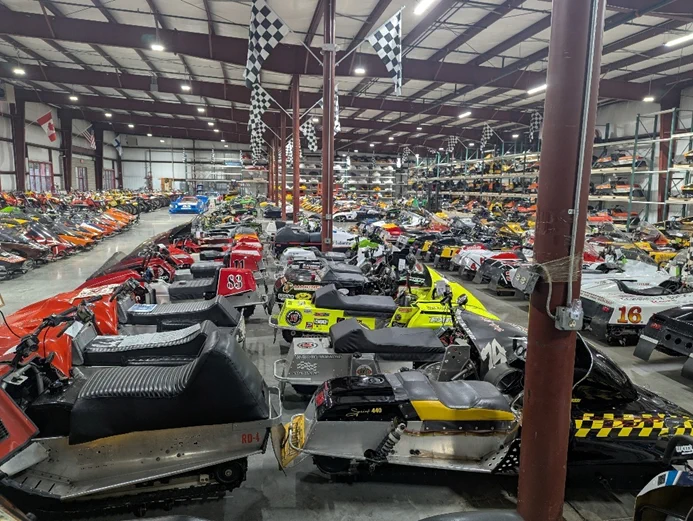  A large number of unidentified vintage snowmobiles located inside a warehouse.  