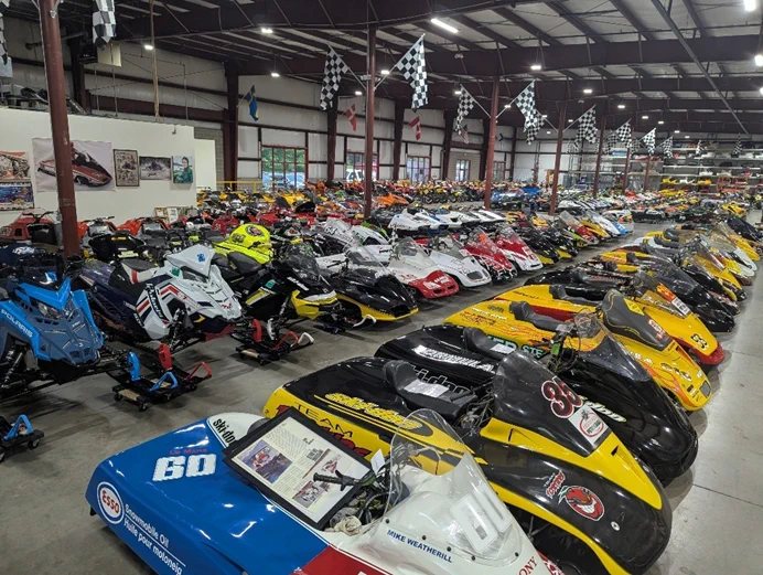  A large number of unidentified vintage snowmobiles located inside a warehouse.  