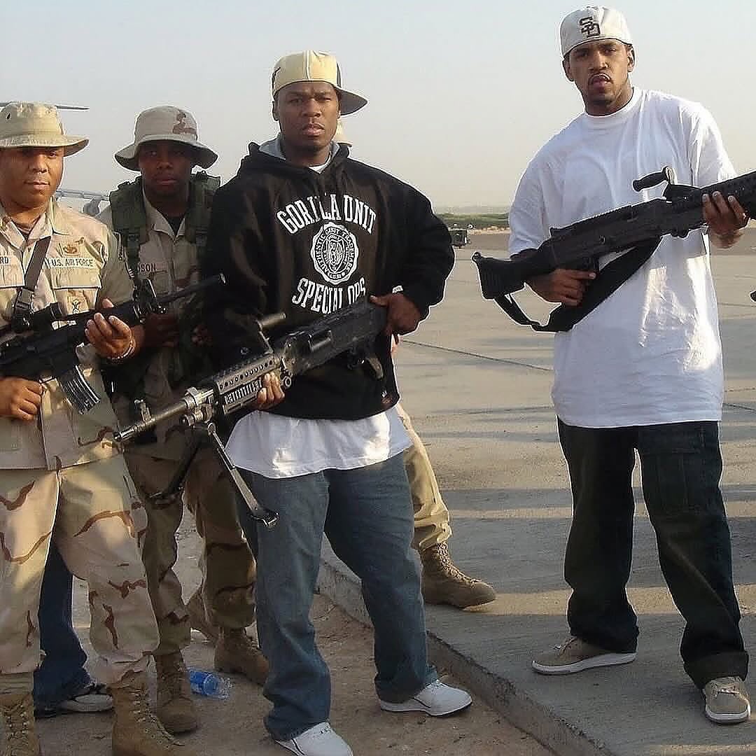 specopsmag's tweet photo. In 2004, during the Iraq War, 50 Cent flew into Camp Anaconda, one of the most dangerous bases in the country, nicknamed "Mortaritaville" because it was getting hit by mortar fire nearly every day. Located near Balad and officially known as Logistics Support Area Anaconda, it was one of the most frequently attacked American installations in the entire country, and reports say the camp had already taken a missile hit on the very day he arrived.

Just hours before he landed, an officer looked at him and told him straight, no BS, that he could die that day. He'd already survived being shot nine times in New York a few years earlier, so he decided to do the show anyway. Wearing a bulletproof vest, surrounded by military personnel, he walked out and opened the set with "What Up Gangsta."

The trip was part of a USO tour meant to boost morale during one of the more brutal stretches of the war, and by every account it did exactly that, a rapper at the absolute peak of his fame choosing to fly into a base most people were desperate to leave, because the guys stationed there deserved a night that felt like something other than incoming fire. A strange, memorable footnote in the long list of ways people found to support the troops during two decades of war.