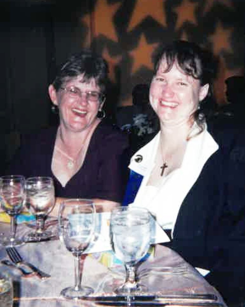Two people sitting at a dining table with several glasses and utensils. They are smiling, and there are star-shaped lights in the background.