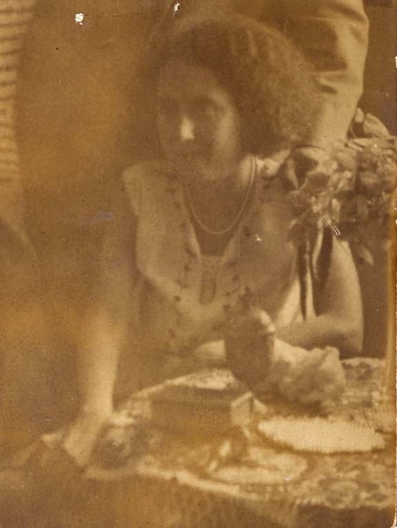 Vintage sepia-toned photograph of a woman seated at a table, looking directly at the camera.