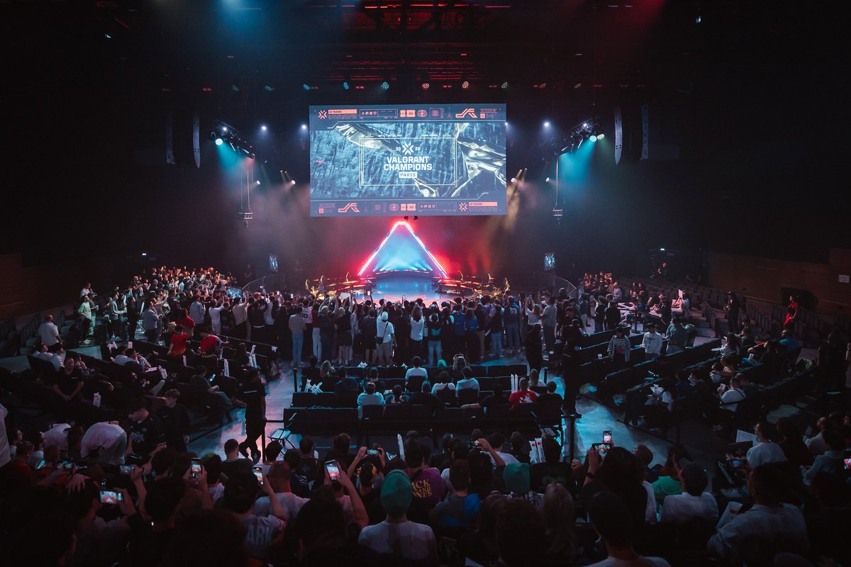 Crowd of VALORANT fans gathered around the illuminated stage at VALORANT Champions Paris, with a large screen displaying “VALORANT Champions Paris” above the arena.