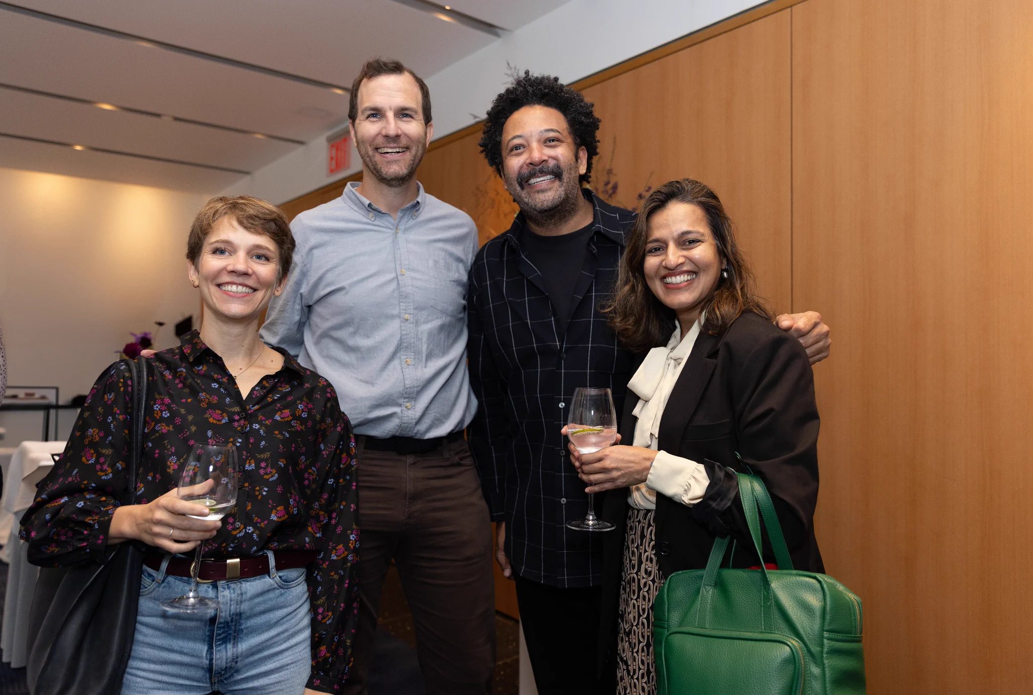 Four people stand in a row, smiling and holding. The two women on the ends hold glasses.