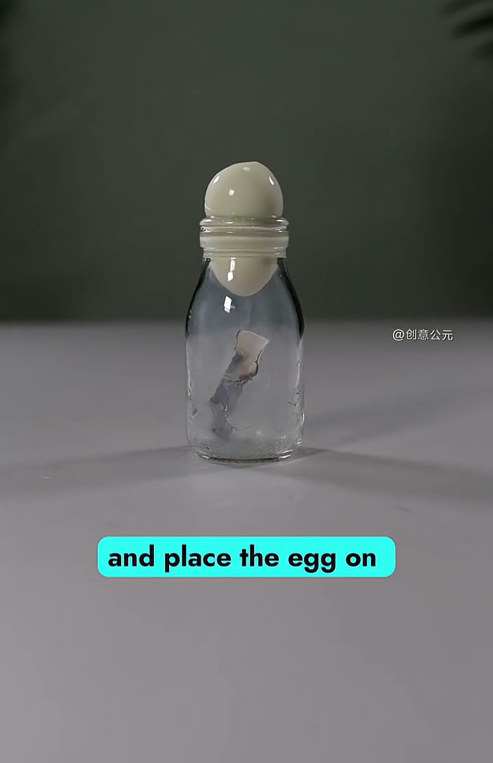 A clear glass bottle containing a peeled egg-like object balanced on its narrow opening, with the caption 'and place the egg on' displayed below.
