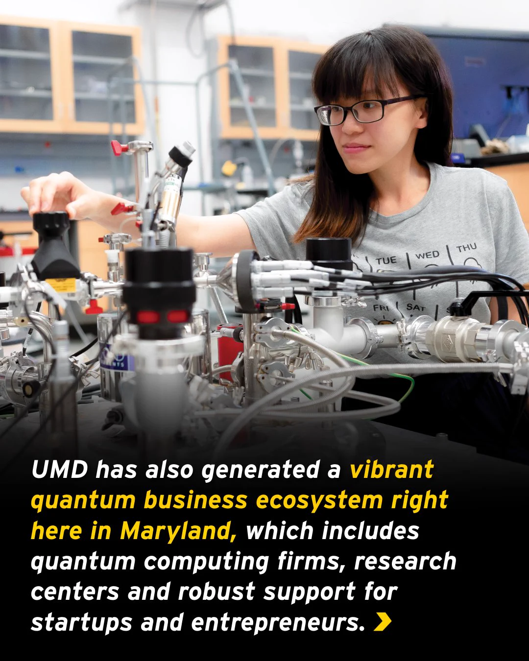 A graphic reads: “UMD has also generated a vibrant quantum business ecosystem right here in Maryland, which includes quantum computing firms, research centers and robust support for startups and entrepreneurs.” In the background is a female researcher operating a device inside a laboratory.