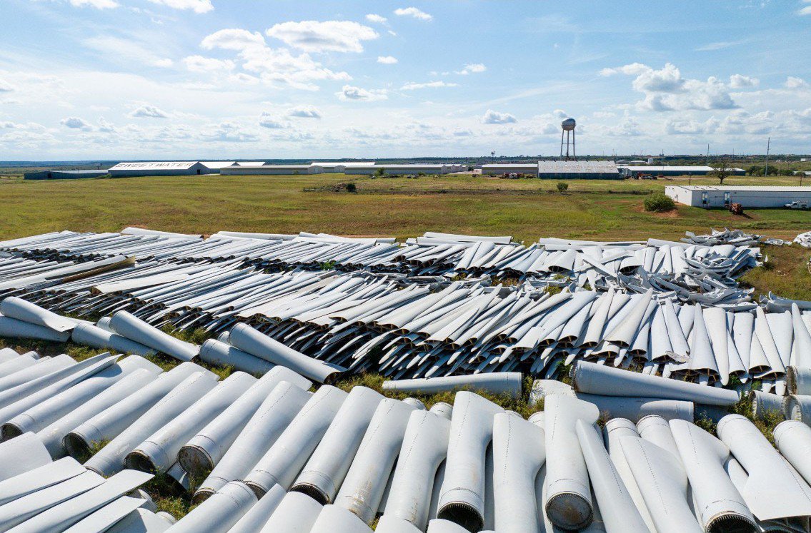 PeterDClack's tweet photo. From early 2026, Germany, Finland, the Netherlands and Austria have pushed to end the practice of burying decommissioned turbine blades in landfill sites.

This left other nations scrambling for alternative solutions, as composite waste is fast becoming a major environmental bottleneck for the world's wind sector.

Landfill prohibitions do not eliminate the underlying waste—they frequently just transfer it. Without universal processing infrastructure, decommissioned components are loaded onto transport for export to plaves like the UK or France, where landfilling or lower-grade disposal is permitted until alternative solutions are developed.

Downcycling attempts—like repurposing blades into sound barriers, pedestrian bridges or playground structures—struggle to match the incoming volume. The largest commercial blades span over 76 meters, longer than the wingspan of a Boeing 747. 

Meanwhile, academic projections indicate cumulative global blade waste will reach 43 million tonnes by 2050, with Europe and North America accounting for a substantial share.

Incineration and traditional chemical recycling introduce their own environmental and economic hurdles. Polymer matrix resins require energy-intensive pyrolysis or solvolysis to free the embedded glass and carbon fibres. In effect, breaking down a 'green' blade demands significant energy inputs, undercutting the net lifecycle emissions savings.

Regulators have begun forcing the issue. EU rules introduced under the Net-Zero Industry Act require wind turbine blades involved in public procurement to meet a minimum 70% recyclability rate. By contrast, France has relied on a progressive quota framework, requiring operators to ensure at least 55% of a rotor blade's mass is recycled or reused.

In response, research initiatives like the EU-funded REWIND project are pursuing industrial-scale recovery—developing methods to spin reclaimed glass fibres into high-value yarn and structural fabrics suitable for secondary manufacturing. 

Commercial trial programs have even begun integrating these decommissioned composite fibres into the electric vehicle supply chain for automotive structural components.

IMAGE: Decommissioned wind turbine blades stored at a facility in Sweetwater, Texas. As European nations restrict traditional landfilling, finding recycling solutions for composite materials is still a global challenge.