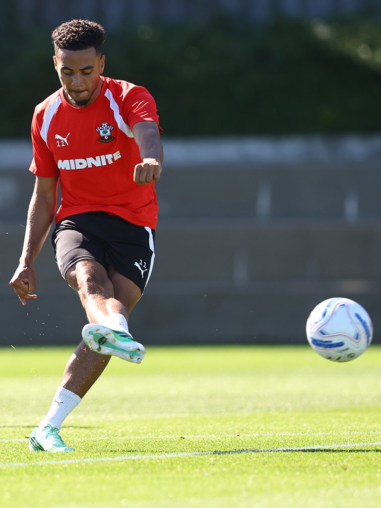 Lewis Dobbin shoots in training with his right foot, wearing a red training top with black shorts and white socks.