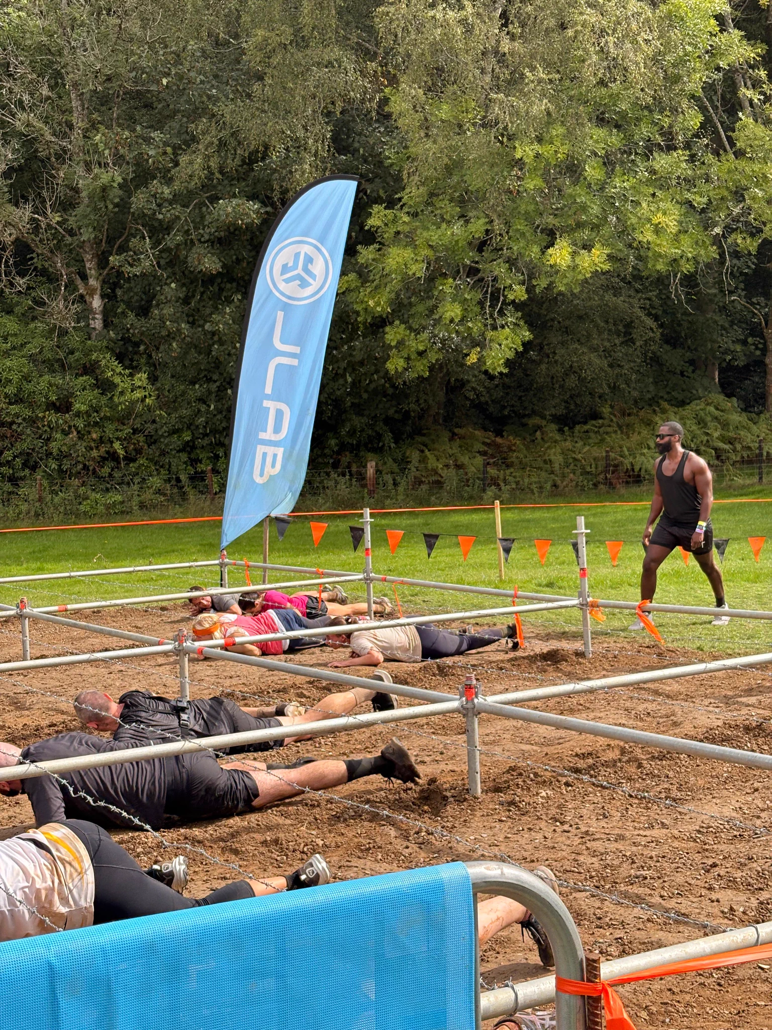 Participants crawling under metal bars through muddy terrain during an outdoor obstacle race event.