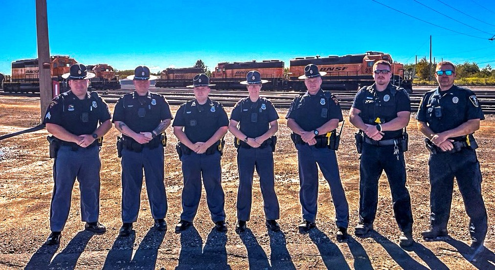 seven members of Wisconsin State Patrol and other law enforcement agencies stand in uniform near railroad tracks