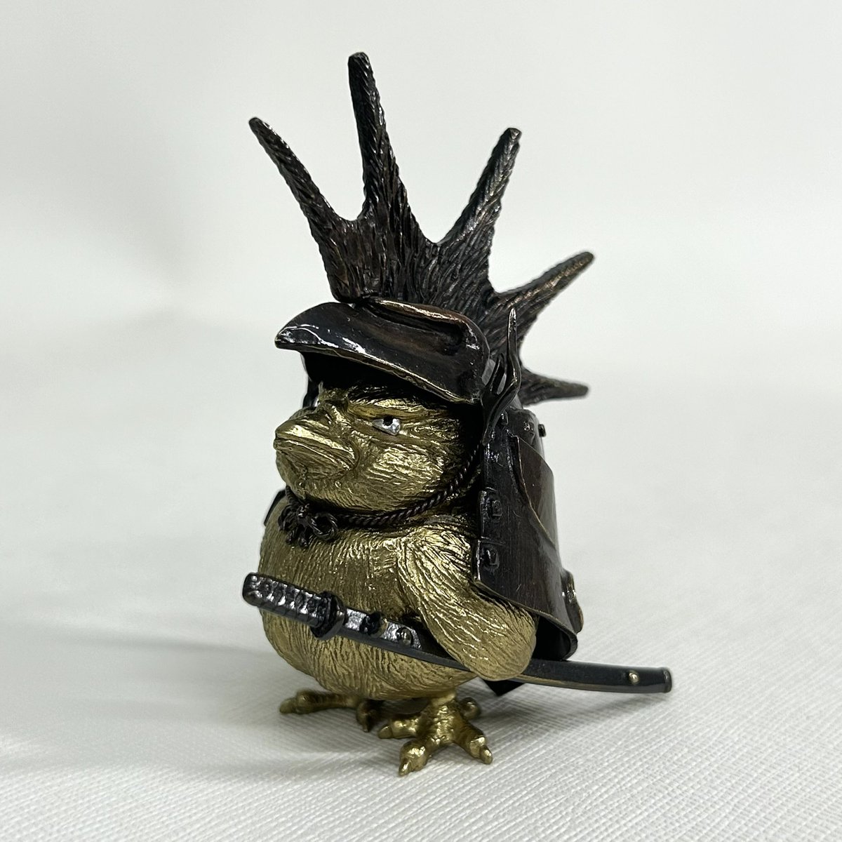 show_mon_art's tweet photo. A small metal sculpture by Yoshiro Iwaisako, featuring a tiny samurai chick.

Freshly hatched, this little warrior wears a samurai helmet, carries a sword, and bravely faces its nemesis.

A slightly oversized helmet, but a fearless little warrior. 

https://t.co/QENjixTe15 https://t.co/uMD4Rcdbvc