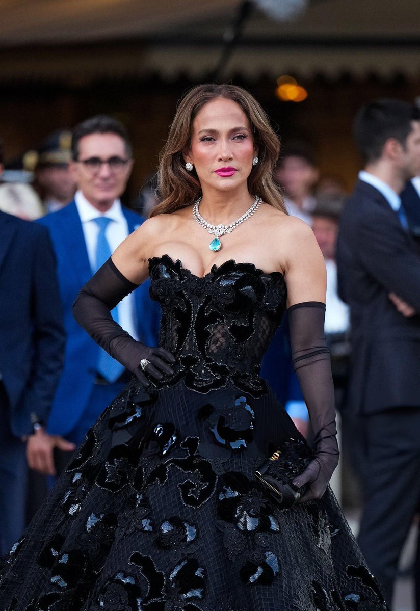 popbuzzz_'s tweet photo. Jennifer Lopez stuns at the Vogue World 2026: Milano in the Galleria Vittorio Emanuele II wearing a strapless black Dolce & Gabbana tulle ballgown with floral sequin appliqués, sheer opera gloves, pointed slingbacks, and a standout 74-carat turquoise pendant necklace.

The star was pulled from the front row by Italian tennis player Lorenzo Musetti for a surprise runway dance moment evoking classic Italian cinema like La Dolce Vita, highlighting the event’s celebration of Made in Italy craftsmanship during Milan Fashion Week.