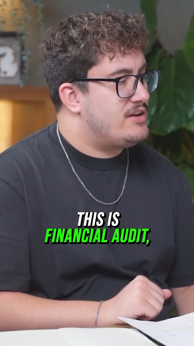 A man with curly hair, glasses, a black t-shirt, and silver chain necklace speaks while looking at papers, with green and white text overlay reading "THIS IS FINANCIAL AUDIT," suggesting this is a clip from the show discussing someone's lavish ring purchase.
