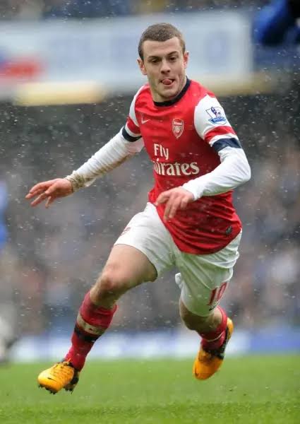 arsenal14japan's tweet photo. 【背番号の向こう側】

ジャック・ウィルシャー
「失った未来を、どう生き直すか」

2011年2月16日。
エミレーツに、当時世界最強と呼ばれたバルセロナがやってきた。

シャビ、イニエスタ、ブスケツ。
前年のワールドカップを制したスペイン代表の心臓部である。

その真ん中に、19歳の少年が立っていた。

ジャック・ウィルシャー。

ボールを受ける。
振り向く。
相手が寄せてくる、その半歩前をすり抜ける。

いつものように、少し舌を出しながら。

考え込んだときに舌が出る人がいる。
彼の場合は、それが世界最高峰の試合中だった。

小さな身体で、何度倒されても起き上がる。
奪われることを怖がらず、またボールを要求する。

アーセナルは2―1で逆転勝利。
試合後、彼の手にはシャビとイニエスタ、二人のユニフォームがあった。

「次のイングランドを背負う選手」

誰もが、そう信じた。

だが未来は、期待された通りには進まなかった。

足首。膝。ふくらはぎ。
復帰しては離脱し、離脱しては戻る。

痛みそのものより苦しかったのは、周囲の目だったのかもしれない。

また怪我か。
身体の管理ができていない。
才能はあったのに。

本人のいない場所で、キャリアは簡単に総括されていく。

もちろん、ウィルシャー自身にも幼さはあった。

FAカップ優勝パレードでは、サングラスにバケットハット姿で宿敵トッテナムを煽り、後に謝罪することになった。

模範的な優等生ではない。
感情的で、負けず嫌いで、時々やりすぎる。

でも、それも彼だった。

ノースロンドンで育ち、アーセナルを愛し、ダービーでは誰より熱くなる。
うまく取り繕えないから、格好いい日も、格好悪い日も、そのまま表に出た。

2013年、ノリッジ戦。

細かいパス交換から、カソルラ、ジルー、ウィルシャーが狭い中央を切り裂く。
最後はジルーのヒールに反応し、ウィルシャーが左足で流し込んだ。

パスが何本つながったかより、全員が同じ景色を見ていたことに息をのむゴールだった。

あれを見た人は、簡単には諦められなかった。

もう一度、この男がピッチの中心に立つところを見たい。

きっと本人も、そうだった。

だが、ウェストハムで出場機会を失い、ボーンマスを離れた後、所属クラブが決まらなくなった。

まだ29歳だった。

かつてバルセロナを相手に輝いた選手が、一人でトレーニングを続ける。
携帯電話は鳴らない。

息子から聞かれた。

「どうして、どのクラブもパパを欲しがらないの？」

父親だから、強く見せたい。
元イングランド代表だから、平気な顔もしたい。

けれど、答えは出なかった。

世の中には、努力すれば報われると信じたい瞬間がある。
一方で、いくら努力しても、欲しかった形では返ってこない時期もある。

ウィルシャーは、その両方を知った。

2022年、デンマークのAGFに加入。
華やかな復活劇ではなかった。

半年後、契約は更新されず、30歳で現役を退いた。

誰かが思い描いた「未来のイングランド代表主将」は、そこにはいなかった。

ただ、彼の人生はそこで終わらなかった。

引退からわずか数日後、アーセナルU-18の監督に就任する。

かつて自分が立っていた場所にいる少年たちと向き合った。

才能があるだけでは足りないこと。
期待される怖さ。
怪我で自分だけ置いていかれる感覚。
周囲の声が、自分の価値まで決めてしまう危うさ。

それを彼は、教科書ではなく自分の傷から知っていた。

指導した世代には、ヌワネリやルイス＝スケリーもいた。

やがてノリッジでトップチームの指導に携わり、2025年には幼少期を過ごしたルートン・タウンの監督に就任。
翌年、ウェンブリーで監督として初めてのトロフィーを掲げた。

選手として思い描いた場所とは違う。
それでも彼は、もう一度ピッチのそばに戻ってきた。

その間には、サッカーより大きな出来事もあった。

幼い娘シエナが心臓の病気と診断され、手術を受けた。

自身も何度も手術台に乗ったウィルシャーは、娘の回復する姿を見て、その強さに驚かされたという。

2025年、彼は娘と同じ心臓病を抱える人々を支えるため、ロンドンマラソンを走った。

現役時代に傷め続けた足首で、42.195キロ。

途中から脚を引きずり、何度も無理だと思った。
21マイル地点には、娘がいた。

手作りのボードには、

「GO DADDY GO」

描かれていたのは、一つの赤いハートだった。

ウィルシャーは泣きながら走った。

息子には、何度も時間を聞かれたらしい。
伝説の選手でも、子どもから見れば、なかなかゴールしない普通のお父さんだった。

5時間2分。

19歳の彼なら、想像もしなかった時間だろう。

あの夜、バルセロナの中盤を駆け抜けた少年は、ずっと順調に走れたわけではない。

止まり、転び、疑われた。
自分でも、もう走れないと思った。

それでも人生は、ときどき目的地を変えながら続いていく。

欲しかった未来に届かなかったことと、
その人生に価値がなかったことは、同じではない。

夢の形が崩れたあとにしか、見つからない役割もある。

タイムラインを開けば、同世代の成功ばかりが目に入る。
自分だけが遅れているように感じる夜もある。

そんな夜には、5時間2分かけてゴールした、かつての天才を思い出してほしい。

速く走れた日だけが、その人の物語ではない。

舌を出しながら世界を驚かせた19歳も、
息子の問いに答えられなかった29歳も、
娘のボードを見て泣いた33歳も、
全部、同じジャック・ウィルシャーだ。

人生には、予定していなかった後半戦がある。

そして案外、そこからのほうが、
その人にしか書けない物語になる。

#セバムコ