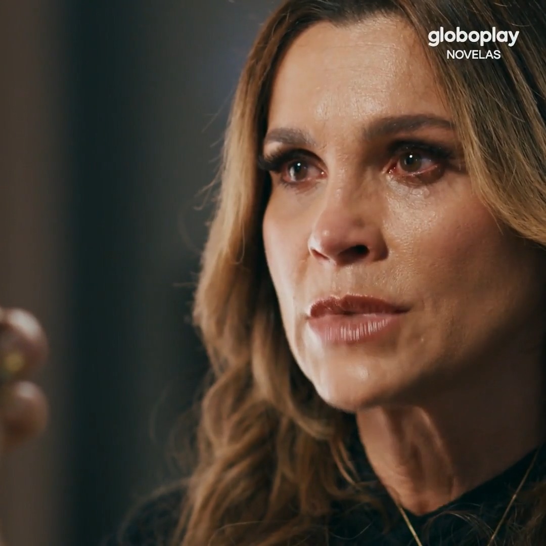 A tearful blonde woman with reddened eyes gazes intensely off-camera in a close-up shot, while the "globoplay NOVELAS" logo appears in the upper right corner. The emotional intensity and dramatic lighting visually reflect the post's narrative of confrontation between Fábia and Pilar, capturing the raw defiance and conflict between the two women.