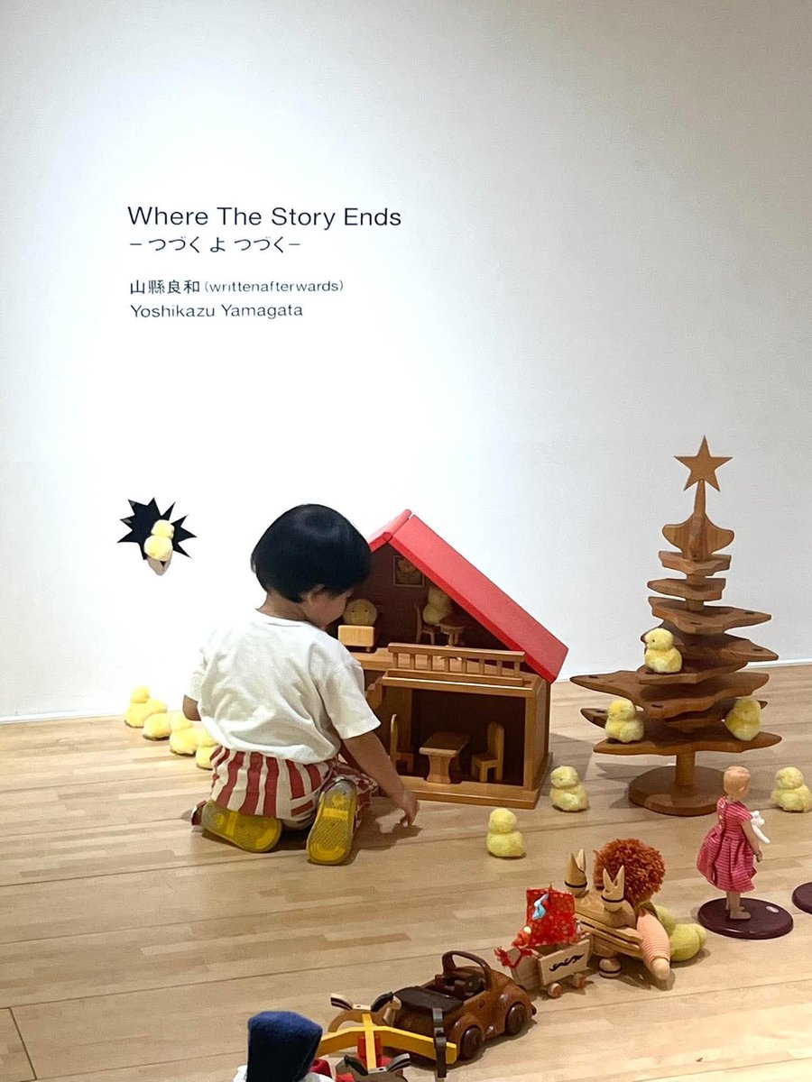 miyamototo's tweet photo. 前橋国際芸術祭2026での山縣良和さんの出品作《Where The Story Ends つづく よ つづく》は、2年前に同じアーツ前橋で僕がキュレーションした大規模個展「ここに いても いい／It`s ALright To Be Here」の続編になっています。山縣さんの息子・綴（つづ）君の成長の歩みが今回のインスタレーションをかたちづくっています。
アーツ前橋の大階段下（プロムナード）に綴君と山縣さんが親子で並べた玩具の行列は、壁を突き抜け、反対側にあるギャラリー４へと続いていくのですが、その先では幼子の無邪気な空想が不穏な異世界へと徐々に変容していきます…。それはこの現実世界の行く末への、山縣さんの（一人の親としての）不安の表出なのかもしれません。
画像1枚目は綴君がアーツ前橋で行列を作っている様子。愛らしい人形や玩具は前橋市中央商店街にある玩具の老舗・黒田人形店の黒田桂子さんからお借りしました。黒田さんには展示制作にあたり様々なご助言をいただき、本当にお世話になりました。writttenafterwards チーム含め、スタッフ一同、心より御礼申し上げます。