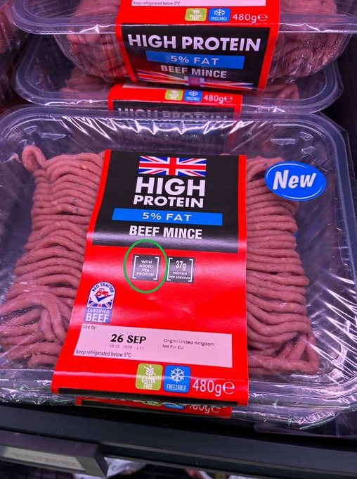 A 480g pack of Lidl's "High Protein" British beef mince sits on a supermarket shelf, marked as 5% fat and "New," with its label highlighted to show the product contains pea protein—a detail central to the backlash over the chain quietly blending plant-based protein into its beef as a cost-cutting and sustainability measure.