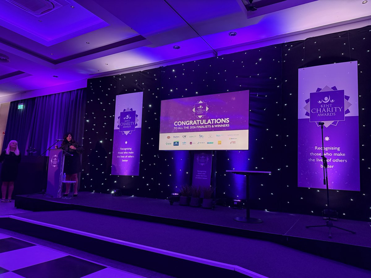 The stage at the Kent Charity Awards lit in purple with two banners and a central projector screen