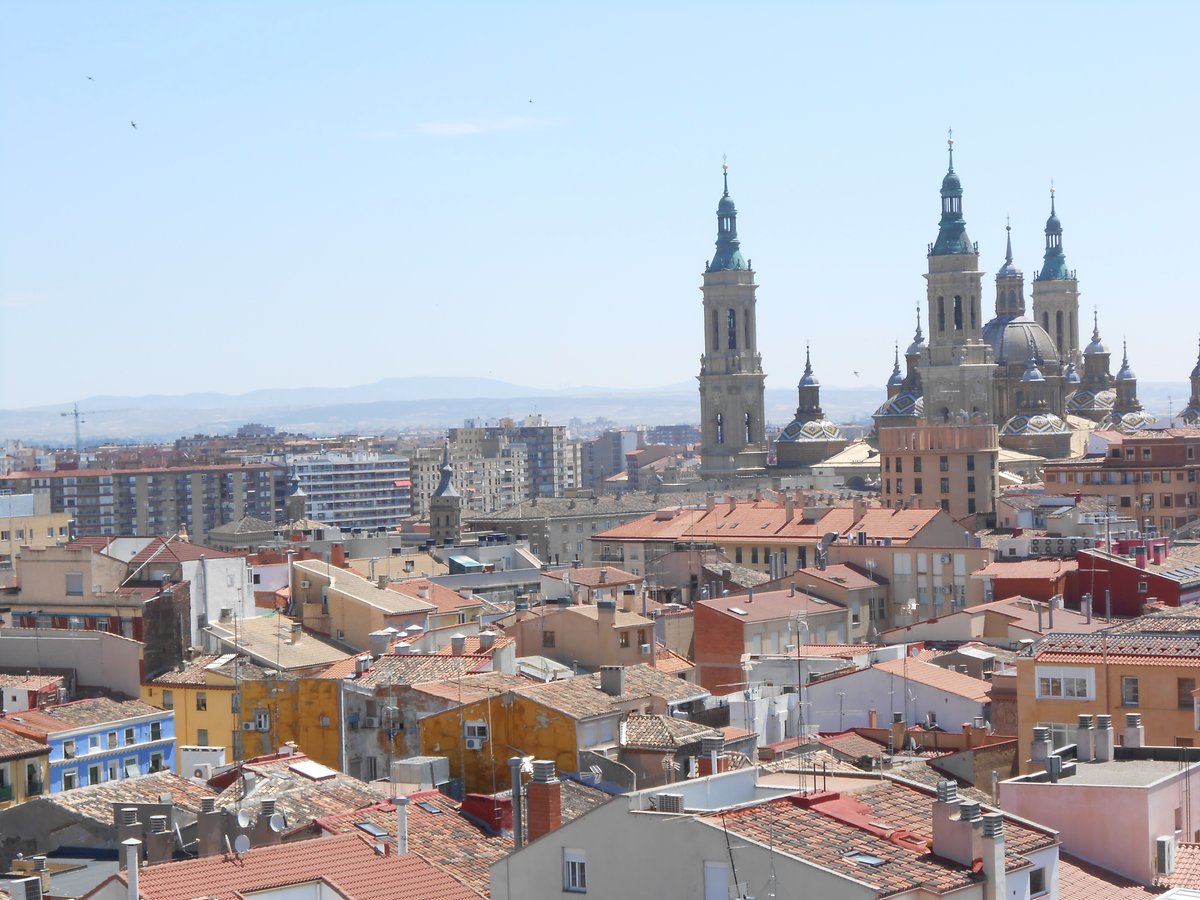Panorámica urbana con tejados rojizos y varias torres y cúpulas de iglesia en el horizonte bajo cielo claro.